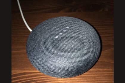 Enceinte Google Nest Mini gris anthracite sur une table en bois, voyants allumés