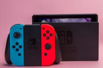 Nintendo Switch avec Joy-Con bleu et rouge devant sa station d’accueil sur fond rose