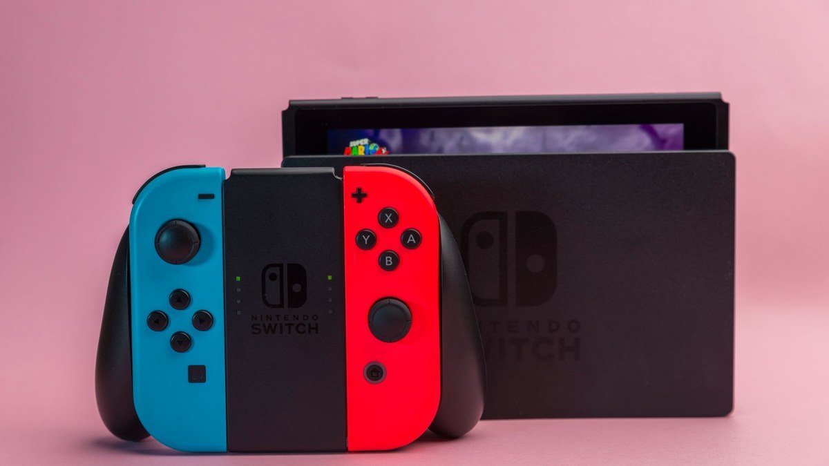 Nintendo Switch avec Joy-Con bleu et rouge devant sa station d’accueil sur fond rose