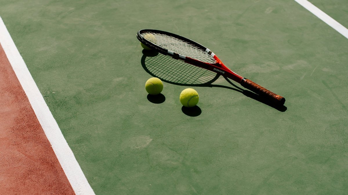 Une raquette et des balles de tennis posées sur un court vert