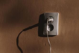 Prise électrique murale avec un câble branché et son ombre sur un mur brun