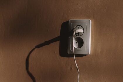 Prise électrique murale avec un câble branché et son ombre sur un mur brun