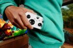 Manette Xbox Nano blanche glissée dans la poche d’un sweat vert