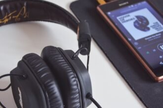 Casque audio noir posé près d’un smartphone affichant un lecteur de musique.