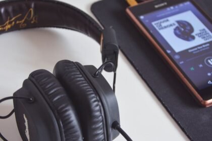 Casque audio noir posé près d’un smartphone affichant un lecteur de musique.