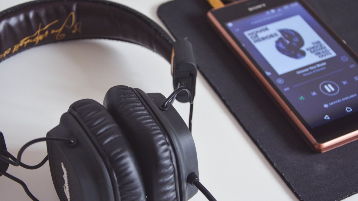 Casque audio noir posé près d’un smartphone affichant un lecteur de musique.